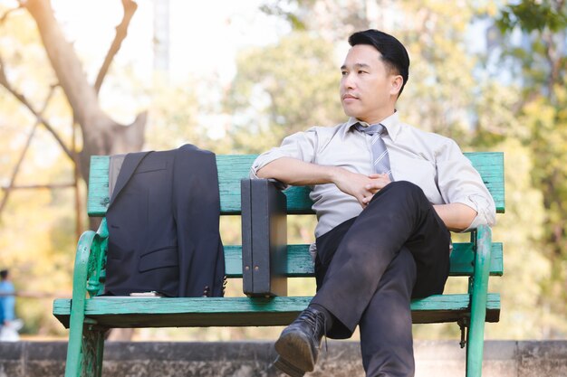 Portrait asian business man sit on a green wooden chair relaxation in park