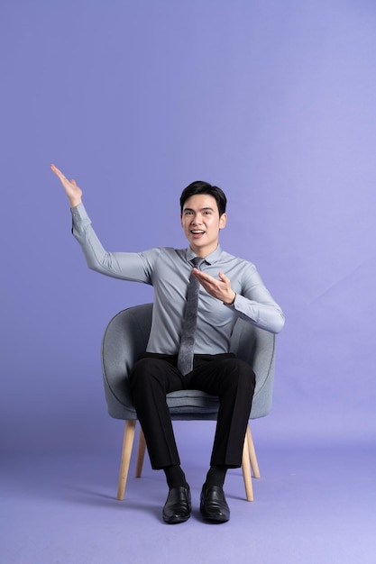 Photo portrait of asian business man sitting on sofa isolated on purple background