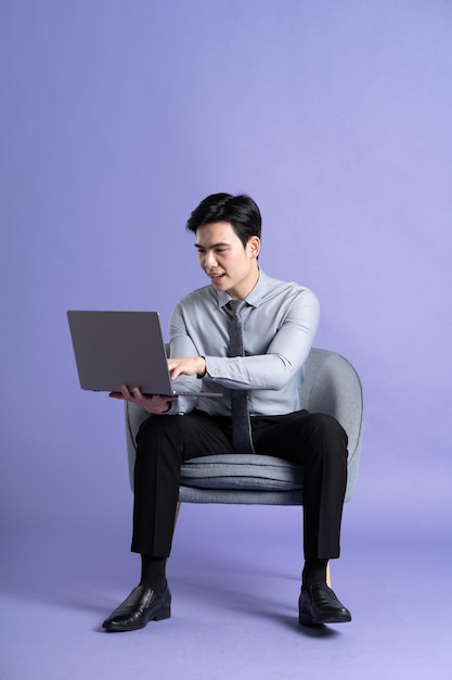 Photo portrait of asian business man sitting on sofa isolated on purple background