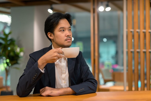 Portrait of Asian businessman in coffee shop drinking coffee while thinking