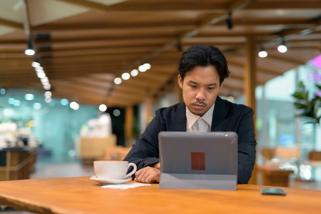 Portrait of Asian businessman in coffee shop using digital tablet computer