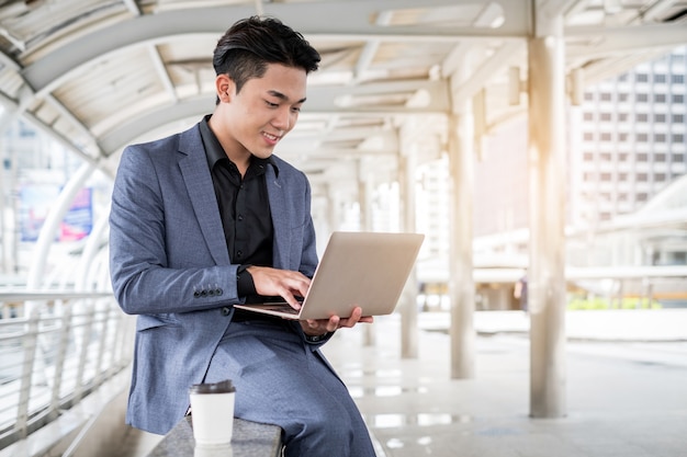 Portrait of Asian businessman holding laptop and coffee cup in the building office city