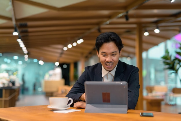 Portrait of Asian businessman sitting in coffee shop using digital tablet computer