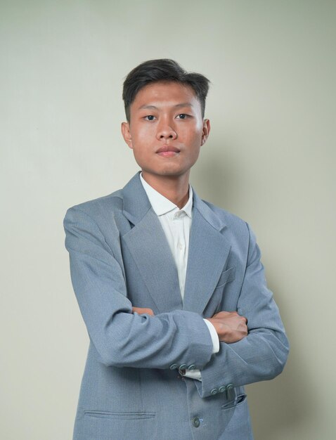 Portrait of asian businessman in suit with arms crossed standing isolated on gray background