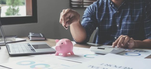 Portrait of an Asian businessman using a calculator to calculate his savings from SME operations with a pink piggy bank as keep money concept