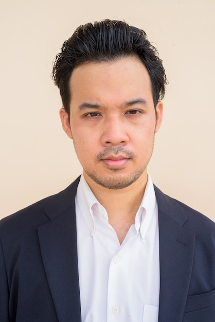 Portrait of Asian businessman wearing suit outdoors against plain background