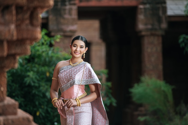 Portrait Asian charming woman wearing beautiful typical Thai dress identity culture of Thailand in ancient temple or famous place with gracefully pose