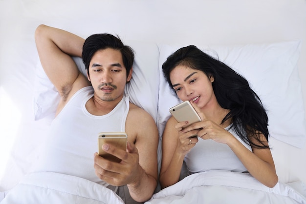 Portrait of asian couple in a bed with smartphones