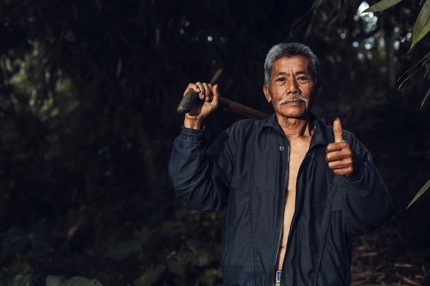 Portrait of Asian farmer man is showing thumbs up and carrying hoe against vintage dark background