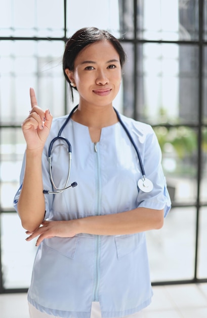 Портрет азиатской женщины-врача, показывающей большие пальцы и улыбающейся