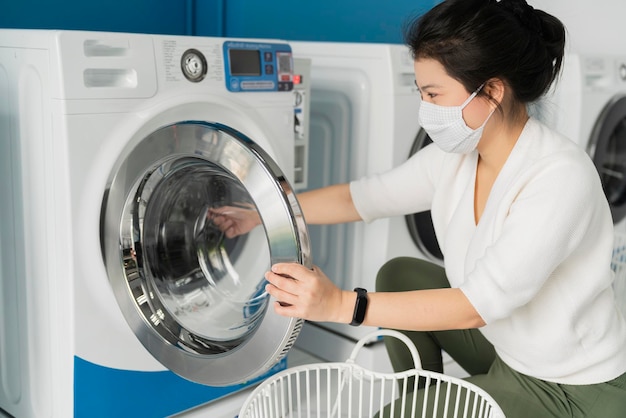 Portrait asian female wear virus protecting mask in spread of covid19 washing in blue color interior laundry shop in condoiminuim city new normal lifestyle