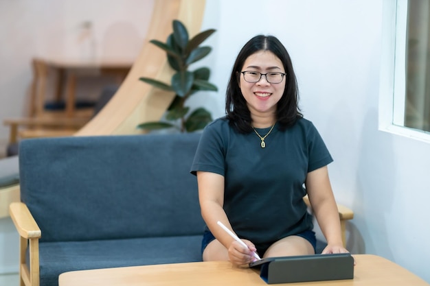 Ritratto di persone freelance asiatiche donne d'affari che indossano occhiali eleganti hipster disegna o prendi nota sulla tavoletta digitale con la penna elettronica per navigare in internet chattando e bloggando nella caffetteria