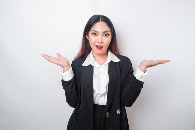 A portrait of an asian girl boss wearing a black suit looks so\
confused between choices isolated by a white background