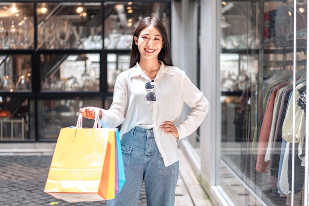 Photo portrait of asian girl excited beautiful girl happy smiling with holding shopping bags relaxed expression positive emotions shopping lifestyle concept