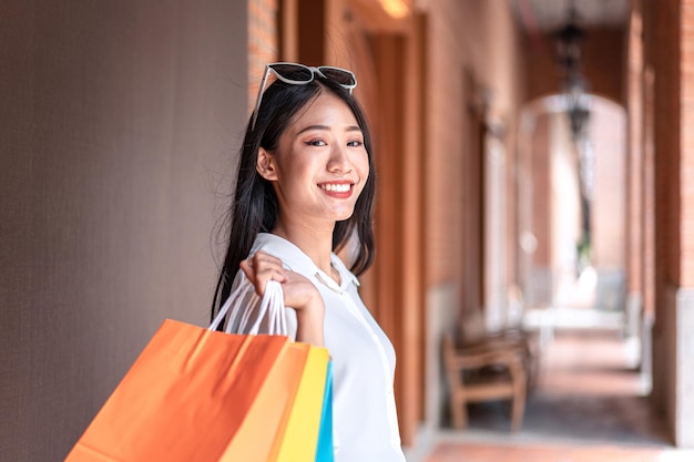 Ritratto di ragazza asiatica eccitato bella ragazza che indossa occhiali da sole sorridendo felice con borse della spesa in possesso godendo nello shopping espressione rilassata emozioni positive concetto di stile di vita di acquisto