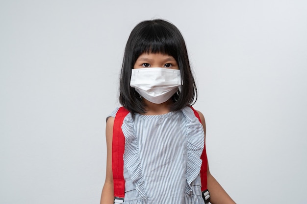 Portrait of asian girl kid with protective face mask and school\
backpack ready for school year