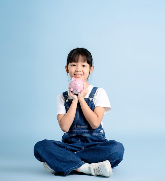 Portrait of asian girl sitting and holding piggy bank on blue background