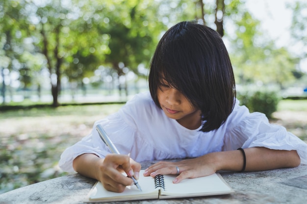 屋外の緑の公園の日記に書かれたアジアの女の子の肖像