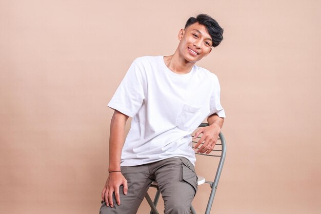 Portrait of Asian Guy Smiling and Sitting at The Bar Chair Isolated on Beige Background