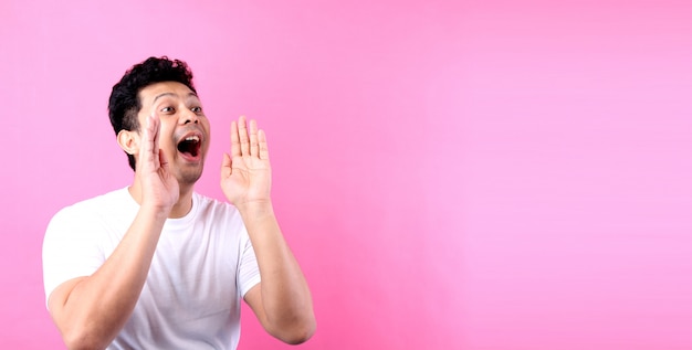 Portrait of Asian guy yelling and hand on his mouth, on pink wall copy space.