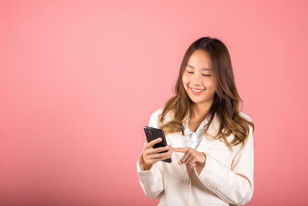 Portrait Asian happy beautiful young woman smile making finger pointing on screen smartphone in hand shopping online application looking to screen, studio shot isolated pink background with copy space