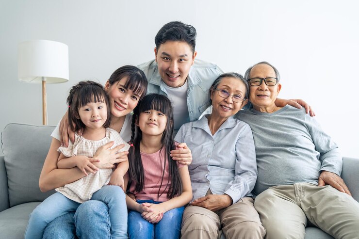 Photo 소파에 앉아서 미소 짓고 카메라를 바라보는 아시아 행복한 가족의 초상화 젊은 부부 부모가 집에서 작은 딸, 형제자매, 노인 할아버지, 할머니와 시간을 보내는 다세대 관계