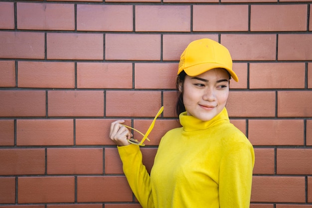 벽돌 벽 배경에 초상화 아시아 힙스터 소녀그녀는 노란색 톤 전신을 입습니다.태국 사람들의 라이프 스타일