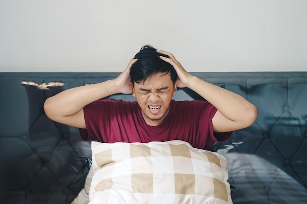 침대에 누워있는 아시아인 인도네시아인 남자의 초상화 머리가 어지럽고 혼란스럽고 우울한 몸짓