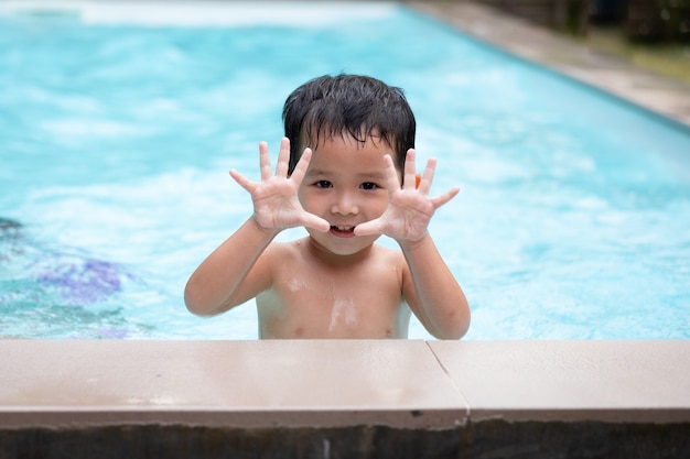 카메라를 보고 수영장에서 물놀이를 하며 웃고 있는 아시아 소년의 초상화. 여름 활동과 어린 시절의 생활 방식 개념.