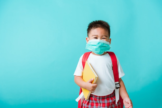 Portrait of Asian little child boy kindergarten wear face mask protective and school bag hold book before going to school