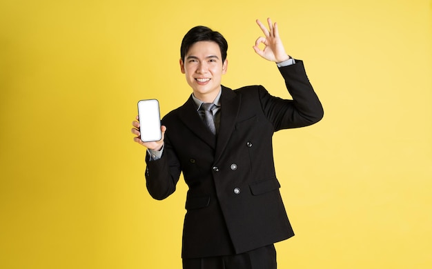Photo portrait of asian male businessman wearing a suit and posing on a yellow background
