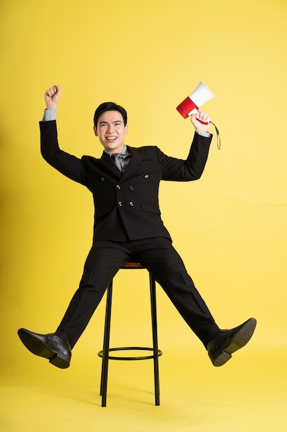 Portrait of Asian male businessman wearing a suit and posing on a yellow background