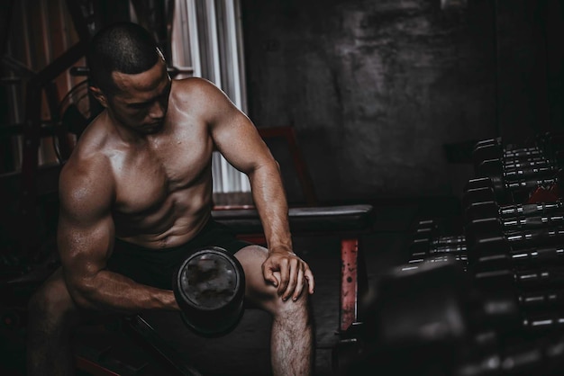 Foto ritratto di uomo asiatico grande muscolo in palestrapopolo thailandeseallenamento per una buona saluteallenamento con il peso corporeofitness in palestra concettoprank ai muscoli addominalisollevare il dumpbell