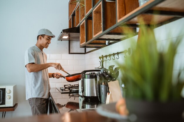 彼自身によって自宅のキッチンで料理をしているアジア人男性の肖像画