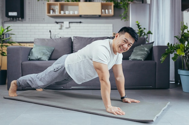 Portrait of an Asian man at home doing fitness and sports at home in the living room on a sports mat pushing off the floor smiling and looking at the camera