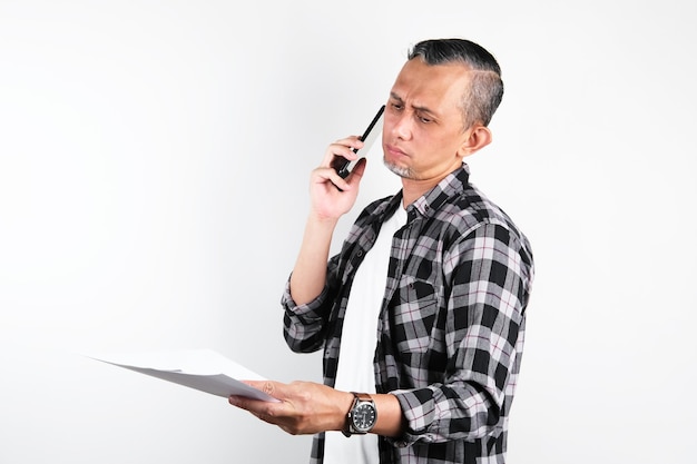 전화하는 동안 실망한 표정으로 빈 백서를 보고 있는 초상화 아시아 남자