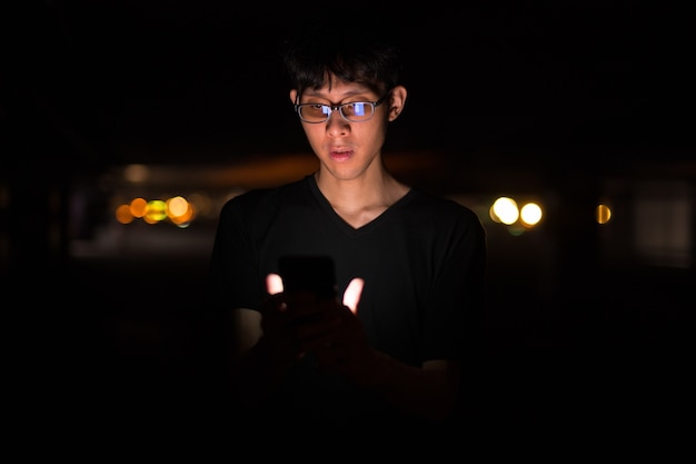 Portrait Of Asian Man Outdoors At Night In Parking Lot Using Mob