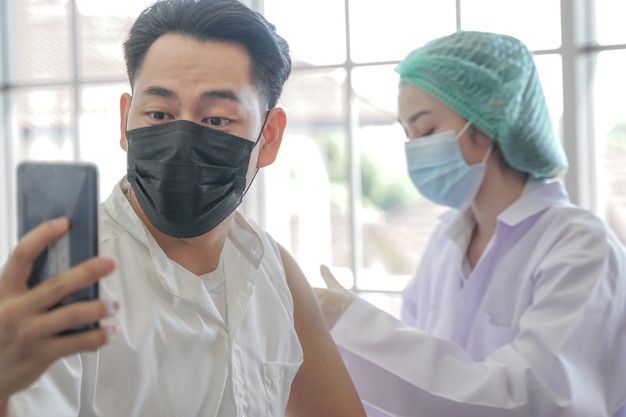 Portrait of Asian man selfie by phone at while getting covid vaccine in clinic or hospital