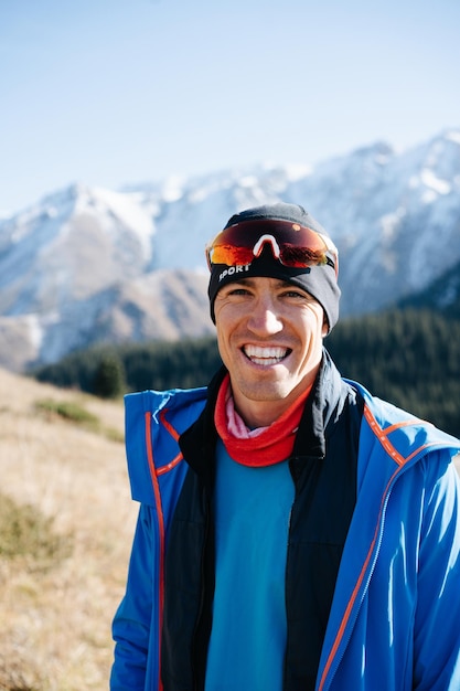 Ritratto di un uomo asiatico in giacca sportiva su montagne innevate sfocate