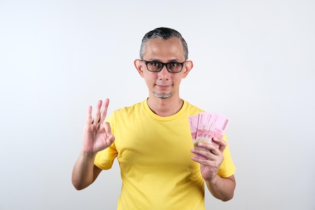 Портрет азиатского мужчины в повседневной рубашке, выглядящего счастливым, держа в руке много денег