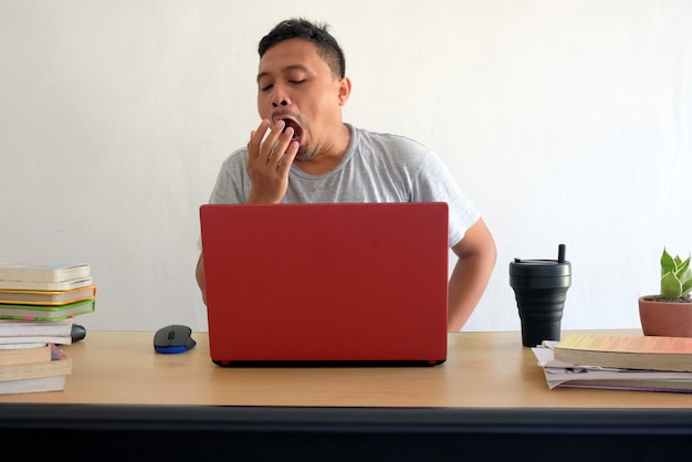 Портрет азиатского человека, зевающего во время работы на ноутбуке