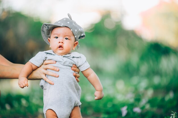 Photo portrait of a asian mother smiling with her 3 months old baby boy on green grass outdoor in  park.