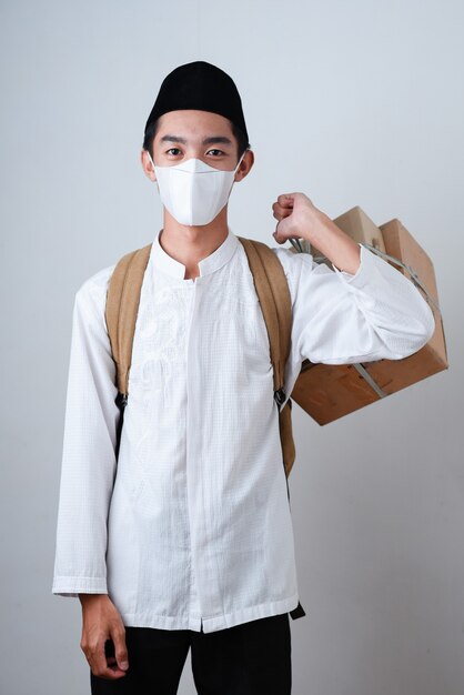 Portrait Asian Muslim man against on grey wearing muslim clothes and holding the box of gifts with a backpack