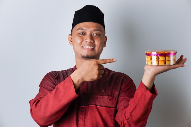 Portrait of an Asian Muslim man holding and pointing to a nastar cookie