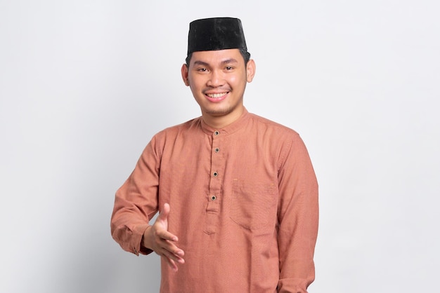 Portrait of Asian Muslim man smiling friendly offering handshake as greeting and welcoming isolated over white background