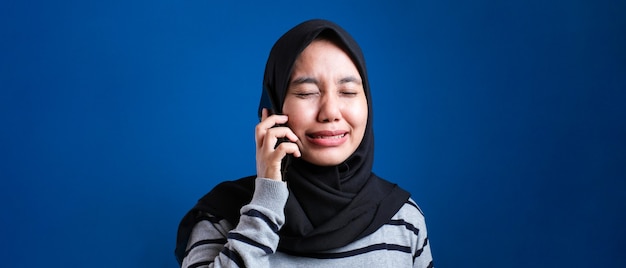 Il ritratto della donna musulmana asiatica riceve cattive notizie al telefono, espressione di pianto triste. su sfondo blu