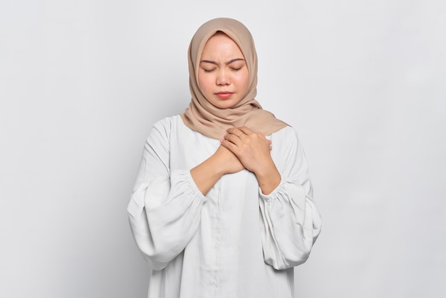 アジアのイスラム教徒の女性の肖像画は心臓発作を起こし、白い背景の上に孤立した目を閉じます