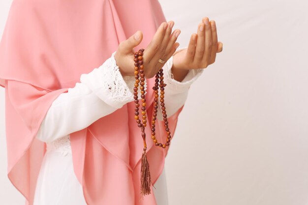 A portrait of asian muslim woman wearing a veil or hijab\
praying with prayer beads on her hand. close up shoot. isolated on\
white background with copy space