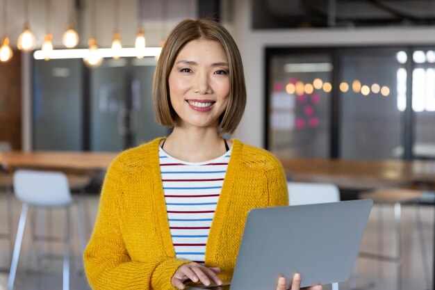 Portrait of asian smiling businesswoman standing holding and using a laptop