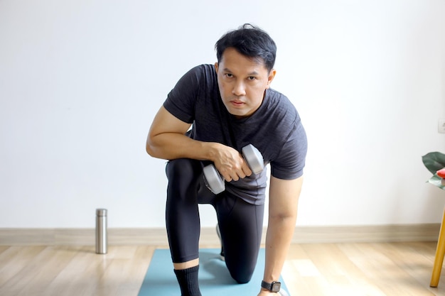 Portrait of Asian sporty man doing dumbbells workout at home working on arms strength